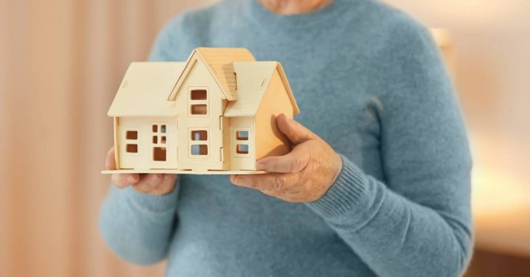 elderly person holding model house